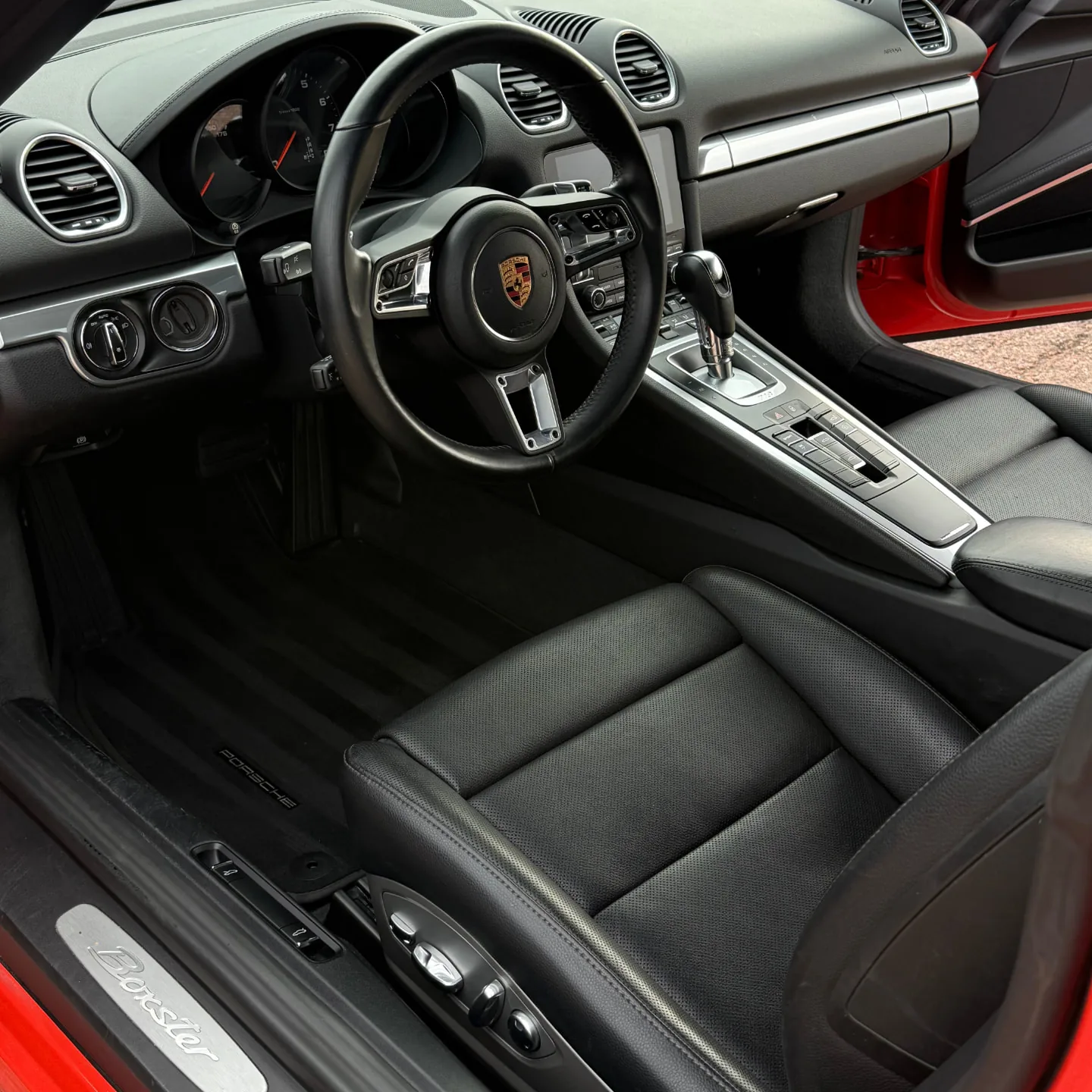 Clean black leather interior of a red Porsche Boxster with the steering wheel, center console and driver's seat after a mobile interior detail in Colorado Springs
