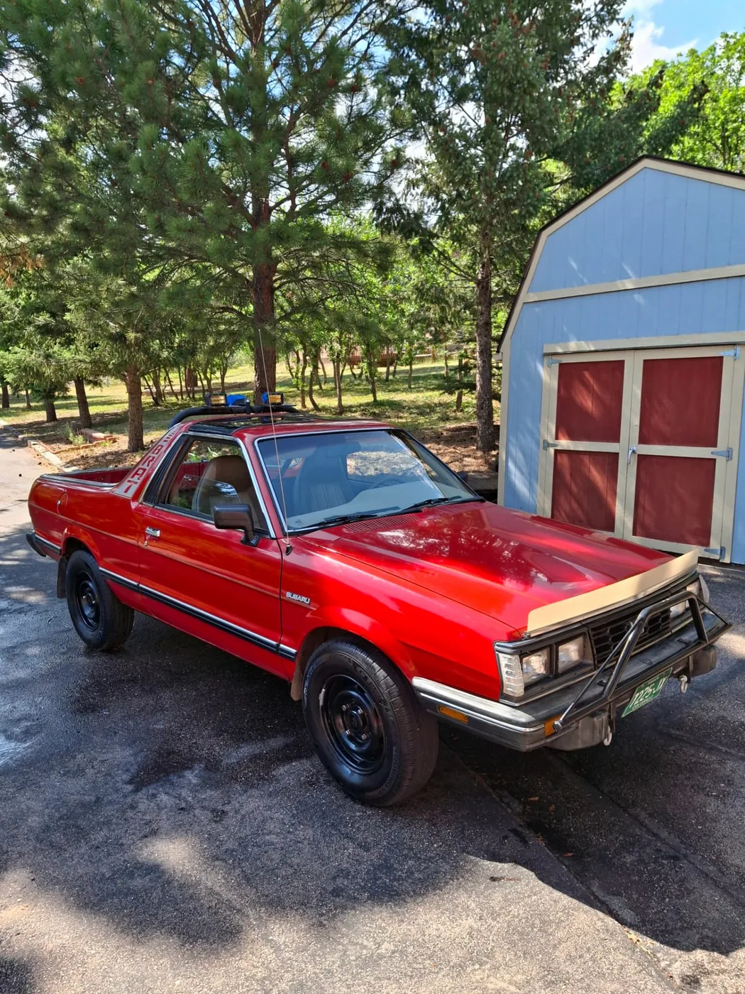 Red classic Subaru BRAT parked beside a blue shed